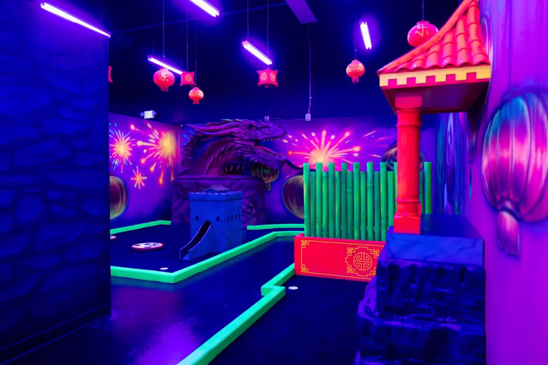 Indoor mini golf course with neon lights, Chinese-themed decorations, red lanterns, and a large dragon animatronic.