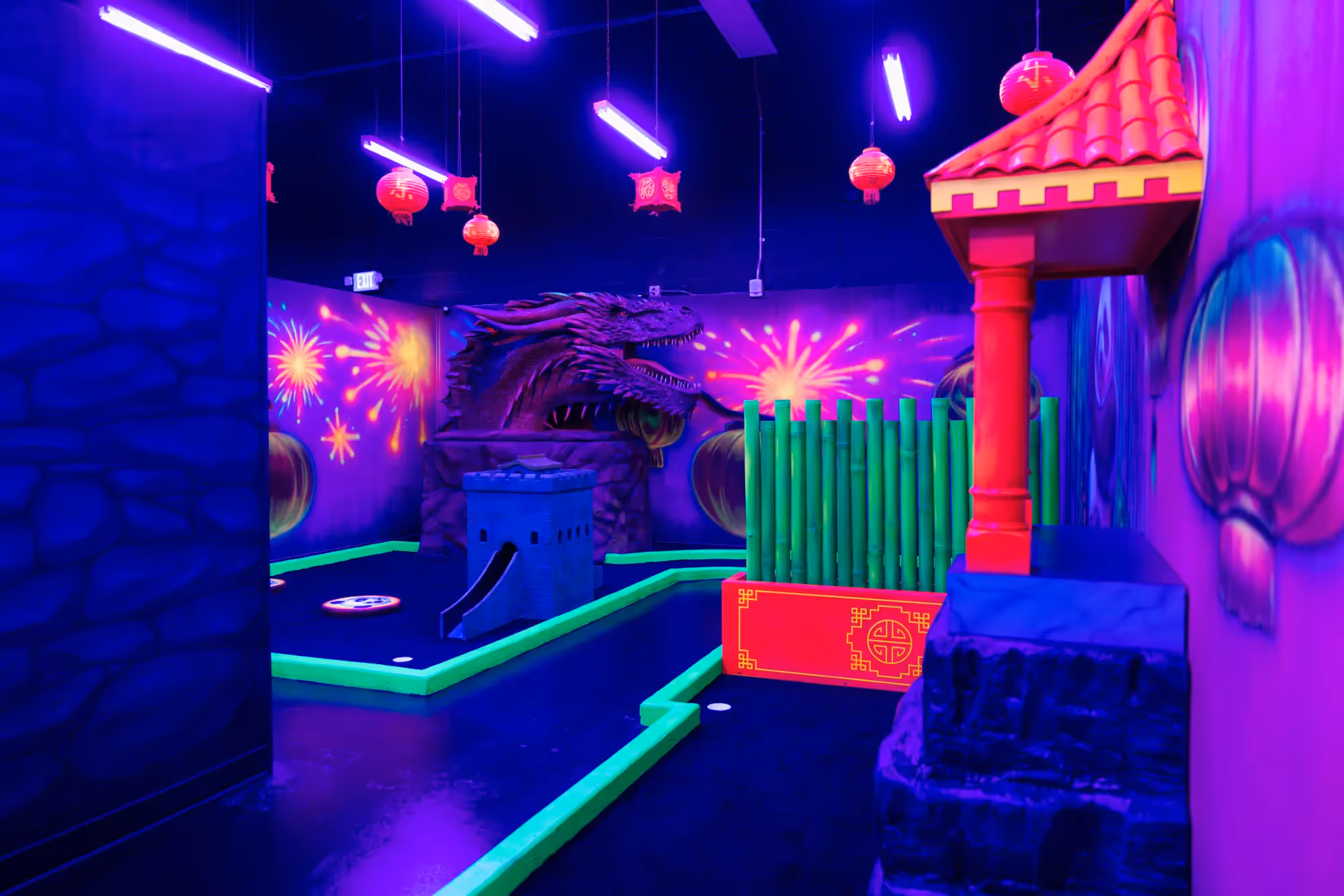 Indoor mini golf course with neon lights, Chinese-themed decorations, red lanterns, and a large dragon animatronic.